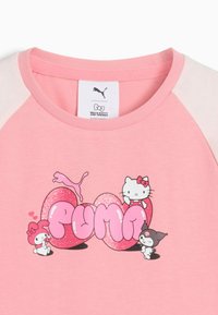 Różowa koszula z błyszczącymi sercami, na których napisano "PUMA", z postaciami Hello Kitty i przyjaciół wokół tekstu.