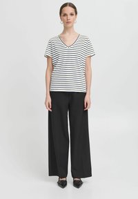 T-shirt a righe a scollo a V in bianco e blu marino abbinato a pantaloni neri a gamba larga. La t-shirt presenta maniche corte e una vestibilità rilassata.