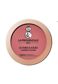 Un compact de blush avec une poudre rose pâle. Présente un boîtier rond brillant en rose doré et un logo noir et vert. Design minimaliste, étiqueté en français.