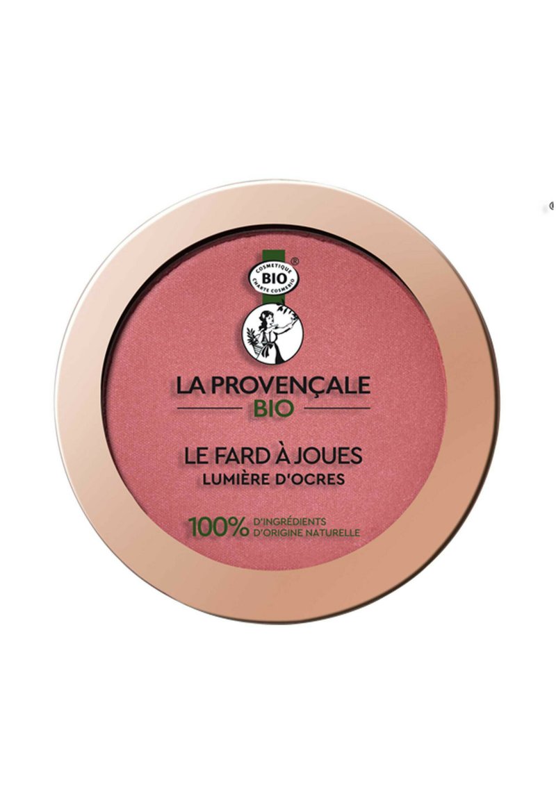 Un compact de blush avec une poudre rose pâle. Présente un boîtier rond brillant en rose doré et un logo noir et vert. Design minimaliste, étiqueté en français.