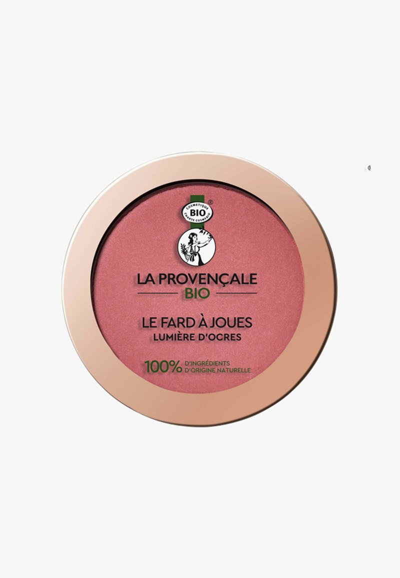 Un compact de blush avec une poudre rose pâle. Présente un boîtier rond brillant en rose doré et un logo noir et vert. Design minimaliste, étiqueté en français.