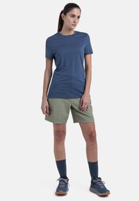 Blå kortærmet skjorte med en glat tekstur, parret med lysegrønne shorts. Mørkeblå sokker og sko fuldender outfittet.