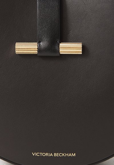 Melnas ādas rokassomu ar zelta detaļām un iekombinētu zīmola nosaukumu. Izceļas ar gludu tekstūru un noapaļotu dizainu.