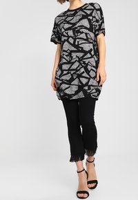 Černé a šedé oversized tričko s abstraktním vzorem a krátkými rukávy, doplněné černými zkrácenými kalhotami s třásněmi na lemu.