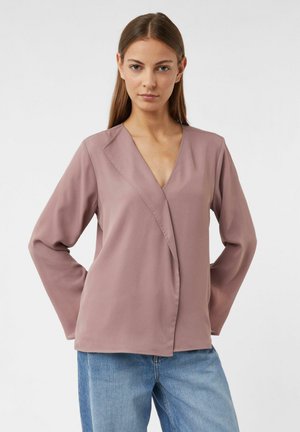 Staubrosa Wickelbluse mit langen Ärmeln, V-Ausschnitt und glatter Textur. Mit einem seitlichen Schlitz und einem entspannten Schnitt, kombiniert mit blauen Jeans.