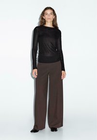 Zwarte langwerpige blouse met hoge taille en wijde, bruine broek. Glad, lichtgewicht stof met een slim-fit silhouet.