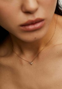 Collar de cadena de oro con un delicado colgante en forma de abeja, acentuado por pequeños cristales, descansando sobre la piel. Diseño simple y elegante.