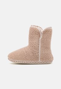 Boot-style slippers made of textured beige yarn, featuring a stitched white geometric pattern along the sole and a subtle peak at the top.
