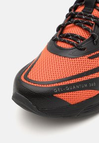Chaussure de course pour homme avec une tige en mesh orange, une semelle en caoutchouc noire et des accents texturés. Présente un logo GEL-QUANTUM 360 bien en évidence.