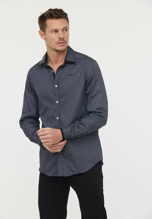 Chemise navy à boutons avec un petit motif géométrique blanc, manches longues et un col noir en accent ; fabriquée en tissu léger.