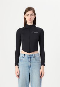 Čierna skrátená mikina so zipsom vyrobená z elastického materiálu s dlhými rukávmi; má vysoký golier a biele logo "JUICY COUTURE".