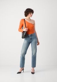 Top arancione a spalla unica, jeans slim-fit in denim azzurro chiaro, tacchi neri a punta e piccola borsa a tracolla nera. Design semplice e attillato con minimi accenti.