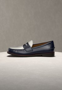 Męskie skórzane mokasyny w granatowym kolorze z białą górą cholewki, z paskiem typu penny oraz niskim, warstwowym obcasem na neutralnym tle.