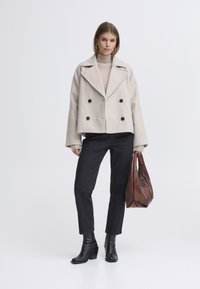Beige wool blend double-breasted jacket with black buttons, paired with black pants and brown leather tote. Black ankle boots complete the look.