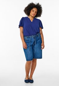 Haut bleu marine à col en V avec de courtes manches volantes, associé à un short en jean bleu ample avec une taille nouée et un détail de couture visible.