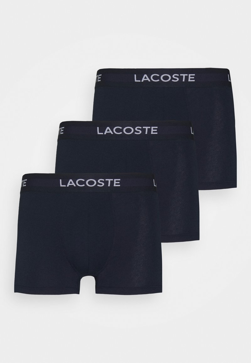 Tres pares de calzoncillos tipo boxers azul marino hechos de suave algodón. Cada uno presenta una cinturilla negra con 'LACOSTE' en letras blancas.