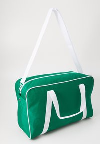Bolsa de deporte verde con cremallera y correas blancas. Forma rectangular, hecha de tela suave. Acentos blancos a lo largo de las costuras y los mangos.