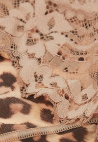 Une bordure en dentelle de couleur beige doux recouvre un tissu à motifs léopard affichant des tons de brun et de beige clair, mettant en valeur des motifs floraux et des textures délicates.