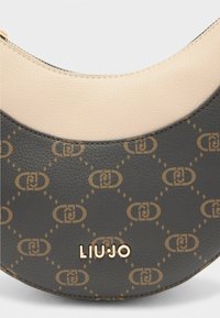Mustard ja beež kahepoolne käekott, millel on tekstureeritud viimistlus, kuldse geomeetrilise mustriga ja kuldse "LIU JO" logo aksessuaari. 