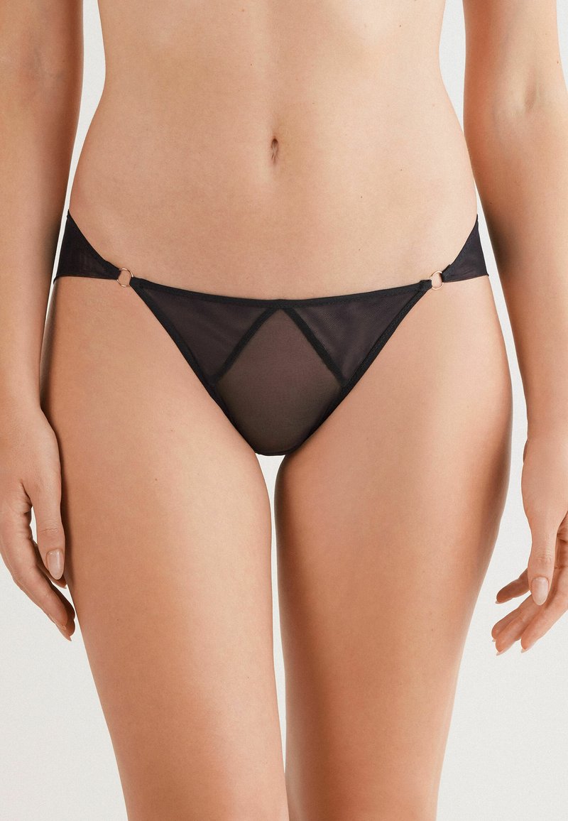 Zwarte mesh bikini onderkant met een driehoekige snit, dunne zijbandjes en kleine goudkleurige ringen als accentdetail.