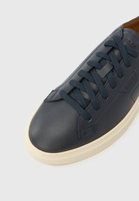 Baskets en cuir bleu marine avec lacets ton sur ton, bout arrondi, semelle en caoutchouc blanche et détail de marque subtil sur le côté. Texture lisse.