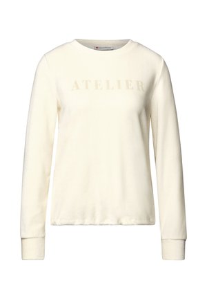 Sweatshirt crème à manches longues en tissu doux avec un col rond. Présente le mot "ATELIER" dans une teinte légèrement plus sombre sur la poitrine.