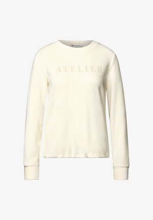 Sweatshirt crème à manches longues en tissu doux avec un col rond. Présente le mot "ATELIER" dans une teinte légèrement plus sombre sur la poitrine.