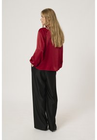 Blusa di raso rosso con maniche a sbuffo, abbinata a pantaloni neri a gamba larga. La blusa ha un orlo arrotondato, creando una silhouette rilassata.