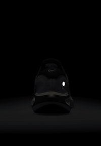 Zadní pohled na černé tenisky Nike s bílou reflexní skvrnou na boku a bílým logem Nike na patní tkaničce na tmavém pozadí.