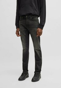 Jeans in denim nero con una vestibilità slim, caratterizzati da un lavaggio scolorito, dettagli cuciti, cinque tasche e una texture usurata, abbinati a sneakers nere.