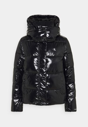 Sort blank puffjakke med høj krave, lynlås foran, sidelommer og lille hvidt Calvin Klein-logo på brystet og ærmet.