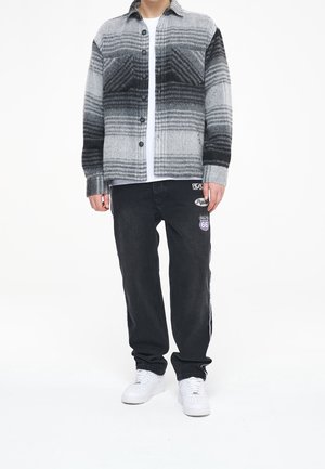 Camicia di flanella a quadri grigi e neri con maniche lunghe, frontale con bottoni e tasche, abbinata a jeans neri con toppe e sneakers bianche.