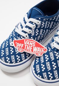Baskets Vans bleues avec des lacets blancs avec logos Vans répétés et motif damier, avec une étiquette logo rouge "Vans Off The Wall".
