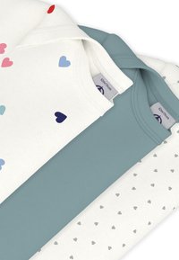 Τρία τοπ στοιβαγμένα. Ένα κρεμ με πολύχρωμες καρδιές, ένα μονόχρωμο γαλάζιο-πράσινο και ένα κρεμ με μικρές γκρι καρδιές. Απαλό ύφασμα. Απλός σχεδιασμός.