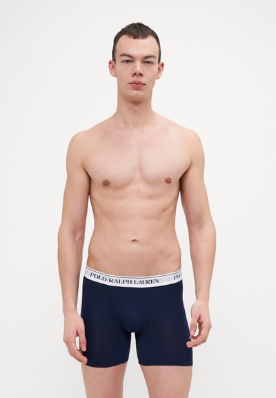 Temno modri bokseric z belim elastik pasom, na katerem je logo "POLO RALPH LAUREN". Tkanina deluje gladko in prilegajoče.