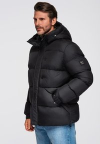 Chaqueta de plumas negra con capucha, que presenta un diseño acolchado, botones a presión y bolsillos laterales. Fabricada con un material suave y duradero.