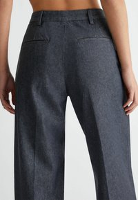 Dark denim trousers with a high waist, featuring two back pockets and a straight-leg design. Smooth texture with subtle fading.