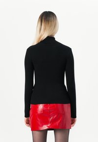 Μαύρος ριβέ γιλέκος με μακριά μανίκια και ψηλό γιακά, συνδυασμένος με μια λαμπερή κόκκινη μίνι φούστα. Απλός σχεδιασμός, χωρίς ορατά σχέδια ή διακοσμητικά στοιχεία.