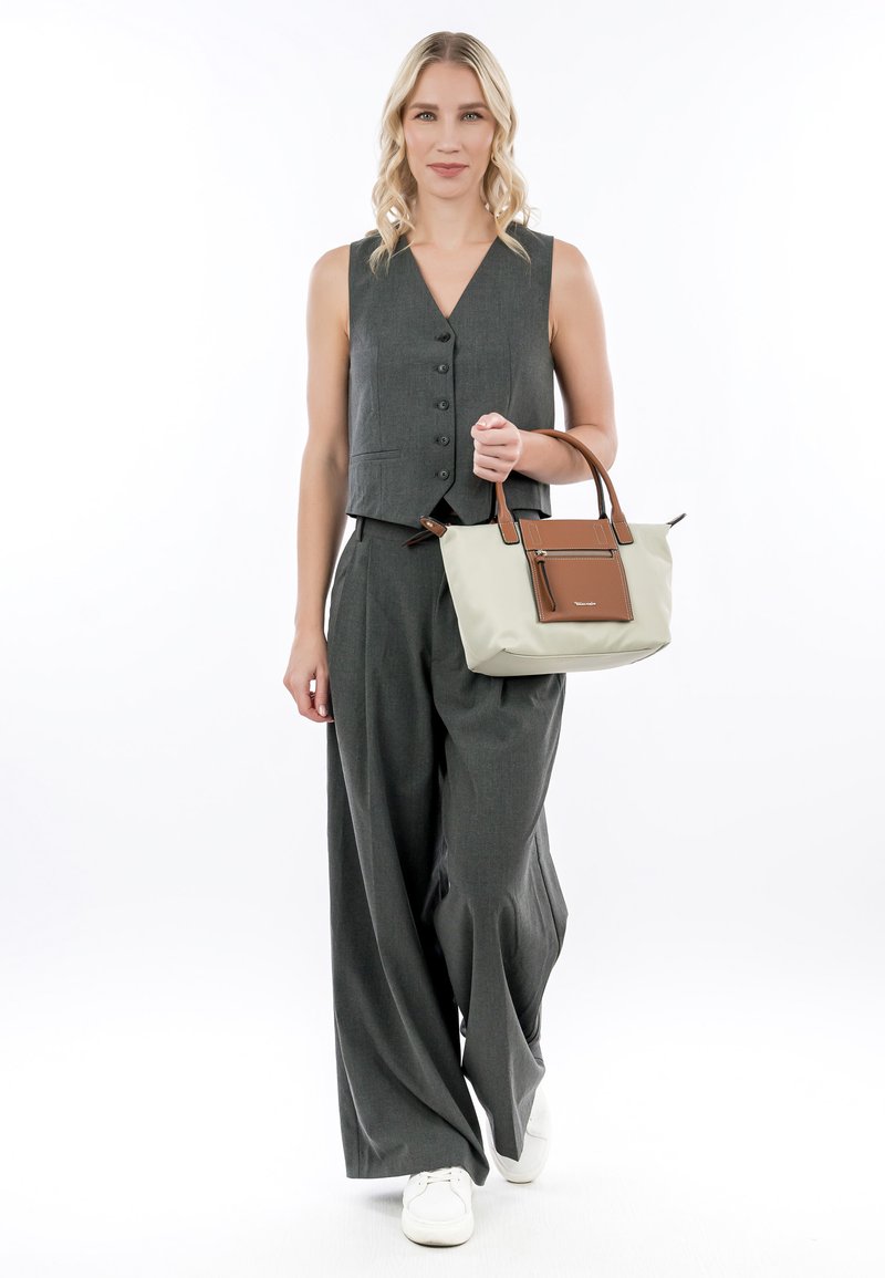 Gilet grigio senza maniche con bottoni frontali, abbinato a pantaloni larghi grigi. Il modello tiene una borsa a spalla beige con un accento marrone.