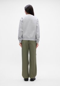 Γκρι φούτερ με ριχτούς καρπούς και στρίφωμα, συνδυασμένο με χαλαρές ελαιοπράσινες παντελόνες. Λεία υφή υφάσματος, με χαλαρή σιλουέτα.