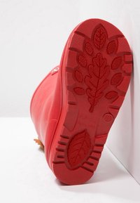 Rød gummistøvle med en struktureret sål, der har et bladmønster og forhøjede dæk. Støvlen har en glat overflade og sideskruer.