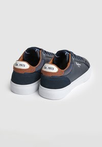 Nizki supergi temno modre barve z belim podplatom, rjavimi poudarki na peti, napisom "Est. 1973" na jezičku na peti in belim logotipom "Pepe Jeans London" na strani.