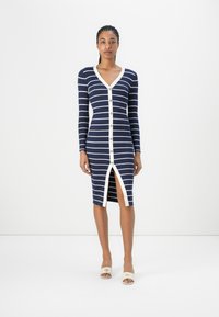 Marine stripet kjole med V-hals, lange ermer og splitt foran, med hvite striper og runde knapper nedover foran.