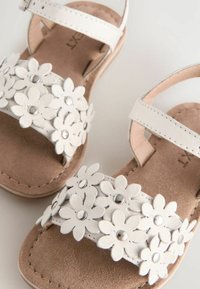 Sandali bianchi con una fascia in pelle floreale e dettagli in argento, una soletta in suede morbido e una cinghia alla caviglia regolabile per una perfetta aderenza.
