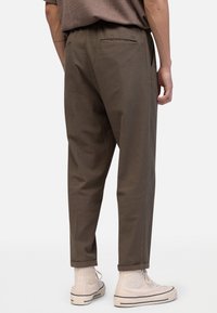 Bruine, loszittende broek met een getextureerd oppervlak, elastische tailleband en een achterzak. Gecombineerd met lichtbeige hoge sneakers.