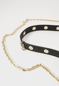 Zwart lederen riem met goudkleurige hardware en ronde accenten, bevestigd aan een gouden ketting. Inclusief een decoratieve bedel.