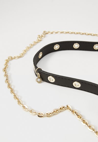 Bracelet en cuir noir avec quincaillerie dorée et accents circulaires, attaché à une chaîne dorée. Inclut un charme décoratif.