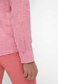 Camicia a maniche lunghe a scacchi rossi e bianchi con polsini abbottonati, caratterizzata da cuciture in contrasto sottili e un tessuto liscio e leggero.