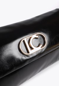 Crna kožna torbica s istaknutim zlatnim logotipom, prikazujući elegantan i moderan stil na praznoj bijeloj pozadini.