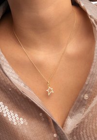 Collana in oro con pendente a forma di stella adornato con piccole gemme trasparenti. La montatura è delicata e presenta una finitura lucida.